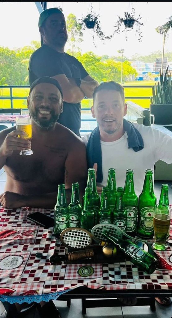 Três amigos na mesa com cervejas e raquetes, no dia em que o torneio foi inventado